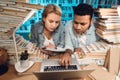 Ethnic indian mixed race guy and white girl surrounded by books in library. Students are using laptop. Royalty Free Stock Photo