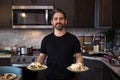 A ethnically mixed male homecook in a kitchen holding plates of eggs benedict. Royalty Free Stock Photo