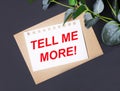 Eucalyptus leaves, an envelope and a white card with the text TELL ME MORE on a dark background. Flat position, top view