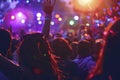 Euphoric crowd with raised hands enjoying a music festival at dusk, vibrant stage lights in the background. Royalty Free Stock Photo