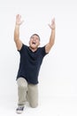 A euphoric middle-aged Asian man in casual attire kneeling and shouting in joy with arms up, isolated on a white background Royalty Free Stock Photo