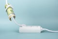 Euro banknote bills tied in knot in electrical power cable and plugged into power strip extension cord on blue