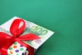 100 Euro banknote on a gift box with a red bow. Green background Royalty Free Stock Photo