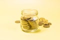 A 5 euro banknote in a glass jar on the background of a scattering of yellow coins.