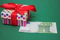 A 100 euro banknote next to a gift box with a red bow. Green background Royalty Free Stock Photo