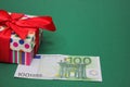 A 100 euro banknote next to a gift box with a red bow. Green background Royalty Free Stock Photo