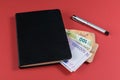 Euro banknotes and fountain pen on red background. Accounting black book Royalty Free Stock Photo