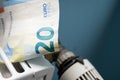 Euro banknotes in a radiator and a thermostat knob at a minimum, close-up. Concept of energy crisis and expensive