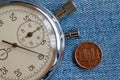 Euro coin with a denomination of 1 euro cent (back side) and stopwatch on blue denim backdrop - business background