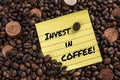 Five cent euro coin over fresh coffee roasted beans and a note with the phrase: invest in coffee