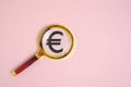 Euro symbol under magnifying glass, on pink background