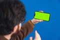 European bearded guy with glasses holding a mobile phone with a mockup green screen in one hand and gesturing with the Royalty Free Stock Photo