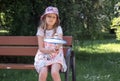 European, blonde, 7-8 years old in a bright panama sits on a park bench