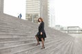 European businesswoman going up on stairs in high buildings background.