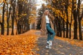 European cute young woman in a fashionable coat in stylish shoes in jeans posing standing on the asphalt in the park on a