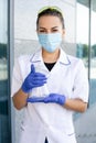 European dark-haired female chemist in medical gown, protective mask and rubber blue gloves holds Erlenmeyer flask Royalty Free Stock Photo