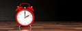 European daylight saving time. Red alarm clock on wooden desk, black background, banner. 3d illustration