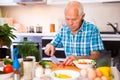 Elderly man cuts vegetables for salad at the table in the kitchen Royalty Free Stock Photo