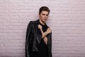 European fashion model of a stylish young man in a fashionable black leather jacket with a trendy hairstyle stands near a vintage Royalty Free Stock Photo