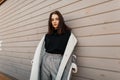 European fashionable young woman model in gray stylish pants in a black shirt in an checkered jacket posing standing