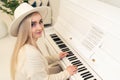 European female blonde long-haired composer in a hat sitting, playing the piano, and looking at camera Royalty Free Stock Photo