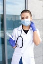 European female doctor with a stethoscope wearing a coat and rubber gloves, putting on a medical mask from viruses Royalty Free Stock Photo