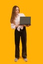 European girl holding laptop computer with blank black screen workspace area. Isolated on yellow background studio portrait. Copy Royalty Free Stock Photo