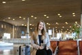 European girl sitting in airport hall with tablet near valise and wearing grey coat. Royalty Free Stock Photo