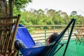 European guy dressed in a blue T-shirt and denim shorts is lying and resting in a blue hammock Royalty Free Stock Photo