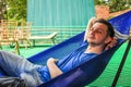 European guy dressed in a blue T-shirt and denim shorts is lying and resting in a blue hammock Royalty Free Stock Photo