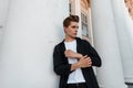 European handsome young man in trendy black shirt in a t-shirt with a stylish hairstyle poses near a white vintage building Royalty Free Stock Photo