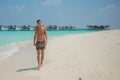 European handsome young tanned man wearing swimming shorts sitting at tropical sandy beach at island luxury resort Royalty Free Stock Photo