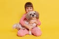 European little girl carrying her pekingese dog and looking directly at camera and smiling, toddler dresses rose clothes embracing Royalty Free Stock Photo