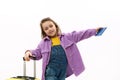 Lovely baby girl in violet velvet jacket, going for holidays, posing with boarding pass and suitcase on white background