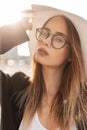 European lovely stylish young woman in vintage glasses in fashionable straw hat in black youth elegant blazer outdoors in city on Royalty Free Stock Photo