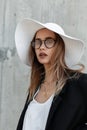 European lovely young girl in stylish glasses in fashionable black-white clothes and summer hat on beach on gray background