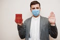 European man in formal wear and face mask, show Latvia passport with stop sign hand. Coronavirus lockdown in Europe country