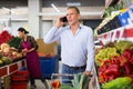 European man shopping in greengrocer and talking on phone. Woman merchandiser working in background.