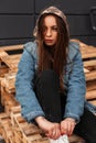 European modern pretty stylish young woman in youth fashionable denim clothes with a military hood posing on wooden pallets