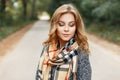 European pretty cute young woman with blond hair in a gray stylish coat with a checkered beige vintage scarf enjoying a weekend