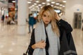 European pretty fashionable young blond woman in an elegant gray coat with a warm vintage scarf with a fashionable leather bag