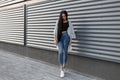 European pretty young stylish woman with gorgeous long hair in fashionable summer clothes is standing near the modern metal wall