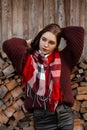 European rural young woman in a knitted stylish sweater with a warm checkered fashion scarf posing outdoors in the village near a Royalty Free Stock Photo