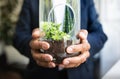 European senior businessman in suit holds glass bottle with microworld plant in office interior