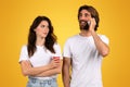 A skeptical woman holding a coffee cup looks askance at a cheerful man talking on a mobile phone Royalty Free Stock Photo