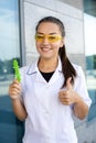 European smiling chemist girl in a white coat and yellow glasses holding green molecules in her hand