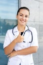 European smiling medic girl in a white coat wearing a stethoscope, showing her thumbs up Royalty Free Stock Photo