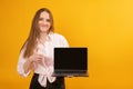 European smiling woman holds laptop with blank screen and showing thumbs up. Studio portrait on yellow background. Copy space, Royalty Free Stock Photo