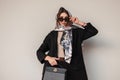 European stylish model young woman in trendy sunglasses in chic fashionable black wear with leather handbag with vintage scarf on Royalty Free Stock Photo