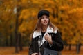 European stylish young woman fashion model in a trendy black hat with a leather bag posing in autumn park on a background of trees Royalty Free Stock Photo